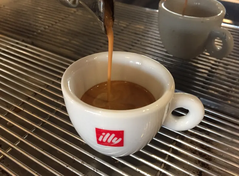 Un espresso illy che scende nella tazzina bianca sulla griglia della macchina del caffè