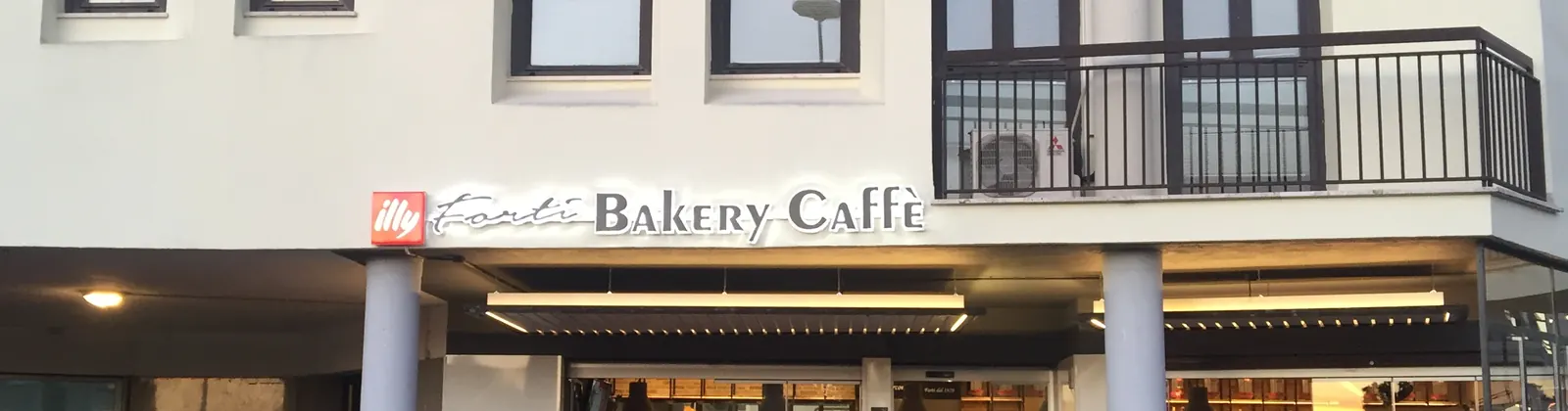 La facciata bianca in Piazza Cina con l'insegna luminosa Forti Bakery Caffè sopra il portico